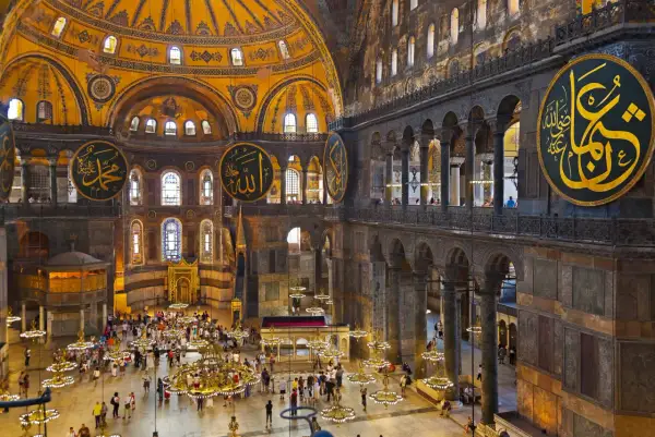 Wnętrze Hagia Sophia z widokiem na kopułę, kaligrafię i turystów. Plan budowli ukazuje jej monumentalność.