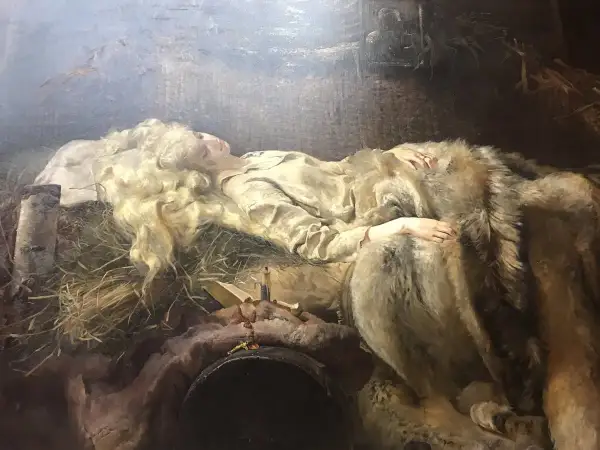 Młoda kobieta o blond włosach, Ellenai, śpi otulona futrem. Obok niej leży krzyż i książka.