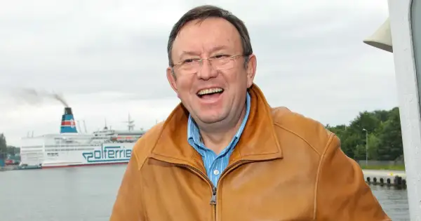 Uśmiechnięty Zbigniew Buczkowski w brązowej kurtce, na tle promu Polferries. Jego filmy, seriale i programy to klasyka polskiej rozrywki.