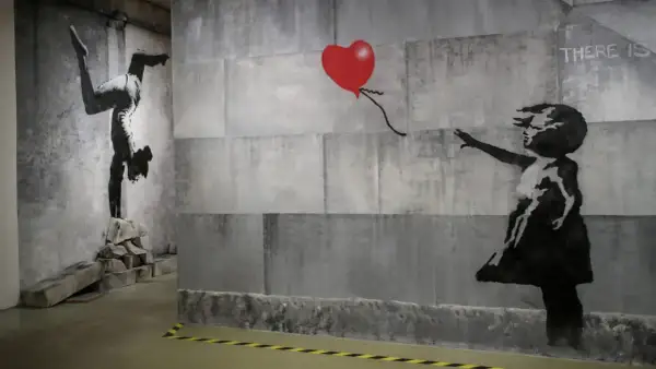 Dzieło Banksy'ego: dziewczynka sięga po czerwone serce, obok gimnastyczka na rękach. Kim jest Banksy? Tajemniczy artysta.
