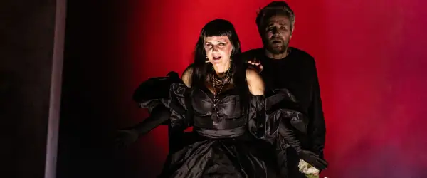 Dramatyczna scena z opery Karola Szymanowskiego. Kobieta w czarnej sukni i mężczyzna z wyrazem przerażenia na twarzy.
