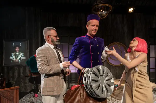 Grzegorz Wiśniewski reżyser, w teatralnej scenografii, z aktorką w różowej peruce i aktorem w garniturze.