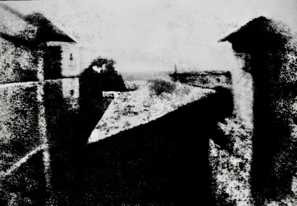 Widok z okna, jeden z pierwszych fotografii. Dachy i budynki w szarościach.