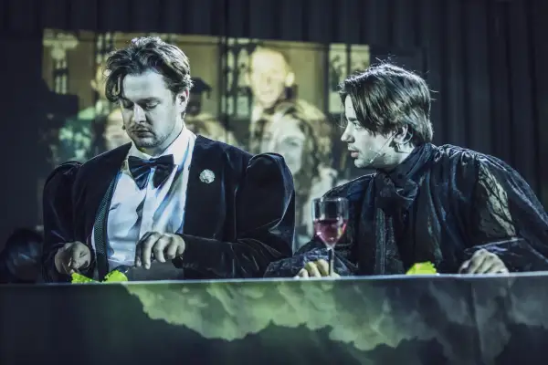 Dwóch mężczyzn przy stole, jeden w czarnym aksamicie, drugi w koronkowej szacie. Może to Hamlet i Ofelia?