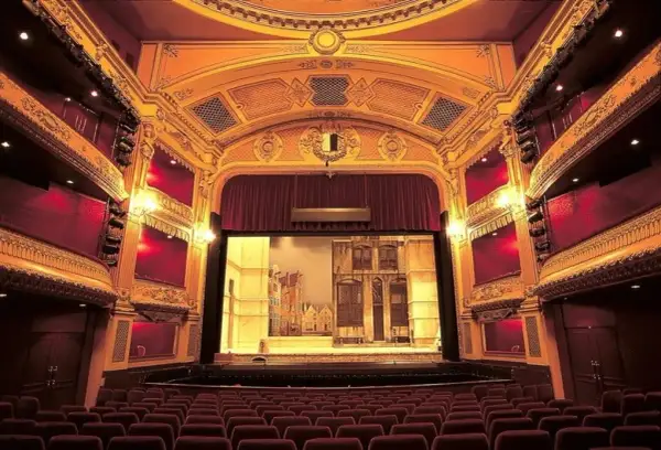 Widok na salę teatralną z rzędami czerwonych foteli i sceną z dekoracjami.