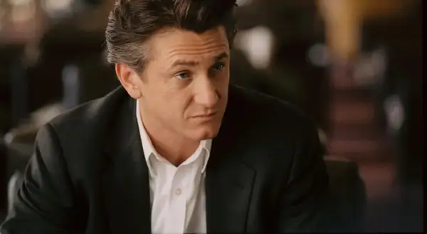 Sean Penn w czarnym garniturze i białej koszuli, zamyślony. Jego role w filmach zapadają w pamięć.