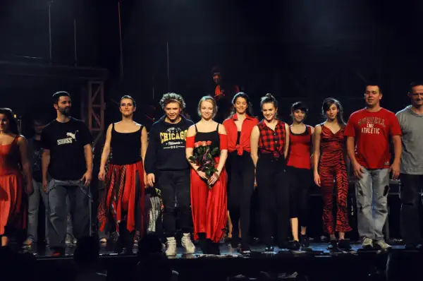 Aktorzy teatru buffo na scenie, w kolorowych strojach, pozdrawiają publiczność.
